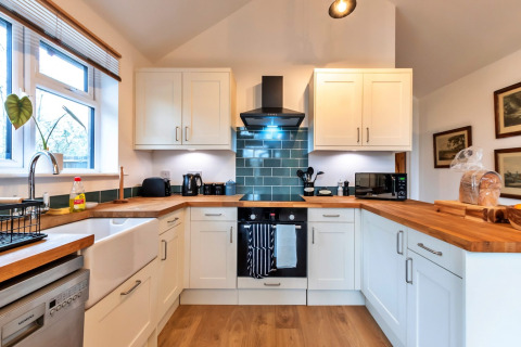 Cucina moderna con mobili bianchi, piani in legno e piastrelle verdi al South Downs Lodge, Regno Unito.