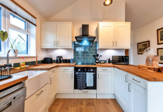 Cucina moderna con mobili bianchi, piani in legno e piastrelle verdi al South Downs Lodge, Regno Unito.