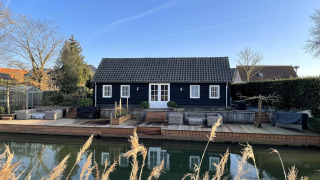 Exterior view of Holiday home De Vlonder with wooden deck by the water and a clear blue sky.