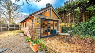 Casa móvil South Downs Lodge con revestimiento de madera, mesa exterior y jardín rodeado de árboles.