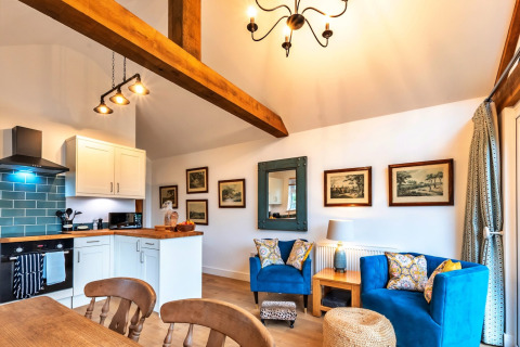 Zona soggiorno luminosa e accogliente a South Downs Lodge, UK, con cucina moderna e poltrone blu vivaci.