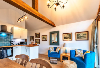 Zona soggiorno luminosa e accogliente a South Downs Lodge, UK, con cucina moderna e poltrone blu vivaci.