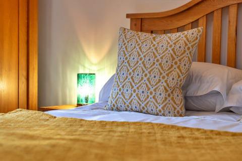 Letto accogliente a South Downs Lodge con cuscino giallo decorato e lampada verde sul comodino.