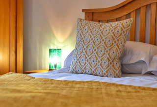 Letto accogliente a South Downs Lodge con cuscino giallo decorato e lampada verde sul comodino.