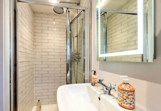 Bagno moderno con doccia, specchio illuminato e lavandino nella casa mobile South Downs Lodge nel Regno Unito.