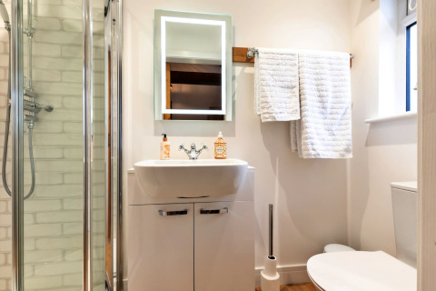 Bagno moderno con doccia, lavandino, specchio illuminato, WC e asciugamani bianchi in una casa mobile.