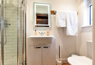 Bagno moderno con doccia, lavandino, specchio illuminato, WC e asciugamani bianchi in una casa mobile.