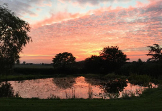Tramonto su uno stagno tranquillo con alberi alla South Downs Lodge, Regno Unito, cielo arancione brillante.