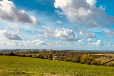 Vista su campi verdi e colline ondulate sotto un cielo azzurro con nuvole vicino a South Downs Lodge, Regno Unito.