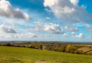 Vista su campi verdi e colline ondulate sotto un cielo azzurro con nuvole vicino a South Downs Lodge, Regno Unito.