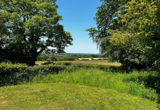 Veduta dal mobilhome South Downs Lodge nel Regno Unito con prati verdi, alberi e cielo sereno d'estate.