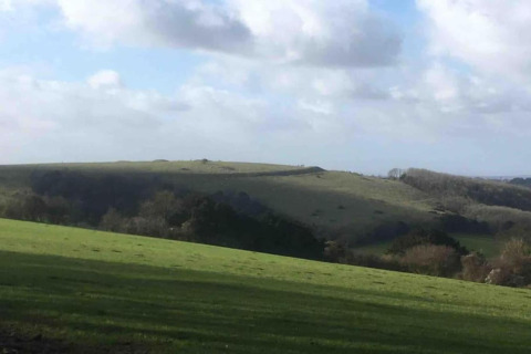 Vista su dolci colline verdi e campi sotto un cielo nuvoloso presso South Downs Lodge, Regno Unito.