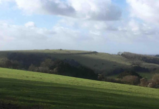 Vista su dolci colline verdi e campi sotto un cielo nuvoloso presso South Downs Lodge, Regno Unito.