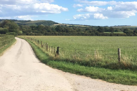 Strada di campagna e campo verde vicino a South Downs Lodge, Regno Unito, con colline e cielo azzurro.