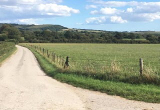 Strada di campagna e campo verde vicino a South Downs Lodge, Regno Unito, con colline e cielo azzurro.