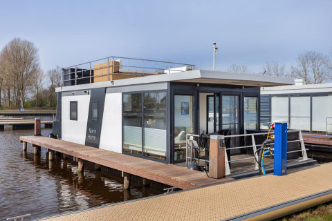 Casa flotante moderna llamada Agua Dolce atracada en un muelle en los Países Bajos, con terraza.