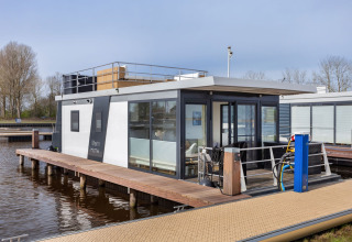 Casa flotante moderna llamada Agua Dolce atracada en un muelle en los Países Bajos, con terraza.