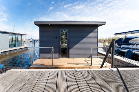 Foto della houseboat 'La Belle Vie' nei Paesi Bassi, ormeggiata al molo con barche e cielo azzurro.