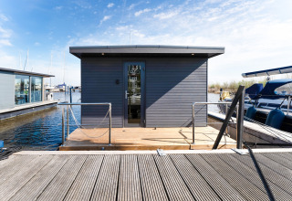 Foto della houseboat 'La Belle Vie' nei Paesi Bassi, ormeggiata al molo con barche e cielo azzurro.