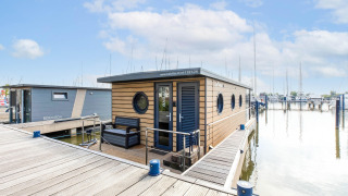 Moderne husbåd ved Volendam Marina, fortøjet ved en bro med udendørs siddeplads under blå himmel.