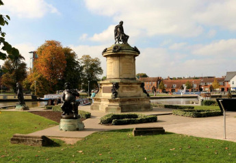 Photo d’un parc au bord de la rivière avec statues et bateaux, prise près d’un hébergement glamping.