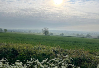 Vue sur des champs verts et fleurs sauvages sous un ciel nuageux près d’un hébergement de glamping.