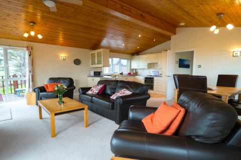 Lichte woonkamer met lederen banken, eetgedeelte en open keuken in Whitsand Bay Lodge, Verenigd Koninkrijk.