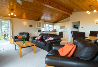 Lichte woonkamer met lederen banken, eetgedeelte en open keuken in Whitsand Bay Lodge, Verenigd Koninkrijk.