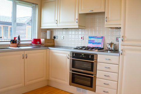 Moderne keuken bij Whitsand Bay Lodge, VK, met witte kasten, gaskookplaat, oven en raam met uitzicht.