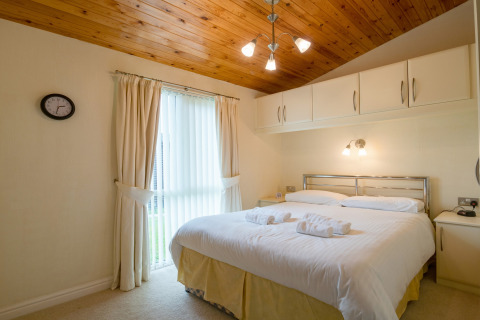 Slaapkamer in Whitsand Bay Lodge, VK, met tweepersoonsbed, houten plafond en ingebouwde witte kasten.