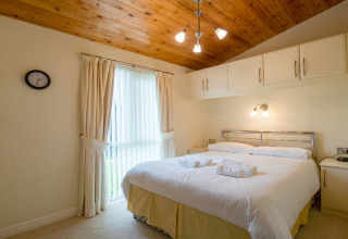 Slaapkamer in Whitsand Bay Lodge, VK, met tweepersoonsbed, houten plafond en ingebouwde witte kasten.
