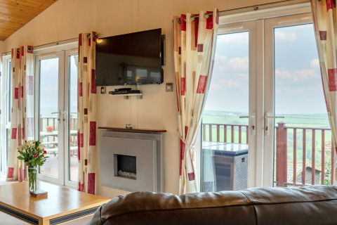 Lichte woonkamer in Whitsand Bay Lodge, VK, met moderne inrichting, tv, open haard en mooi uitzicht.