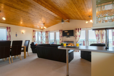 Woonkamer in Whitsand Bay Lodge, VK, met houten plafond, banken, eettafel en ramen met zeezicht.