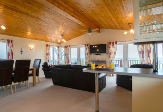 Woonkamer in Whitsand Bay Lodge, VK, met houten plafond, banken, eettafel en ramen met zeezicht.