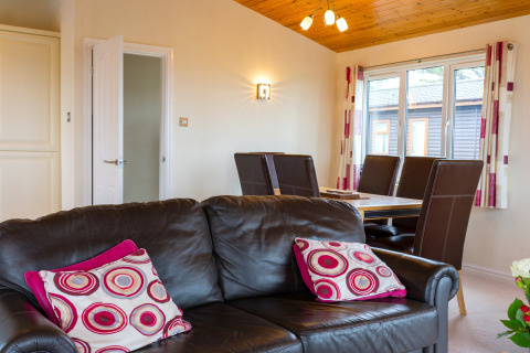 Woonkamer in Whitsand Bay Lodge, VK, met bruine leren bank, eettafel en grote ramen met veel licht.