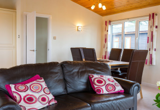 Woonkamer in Whitsand Bay Lodge, VK, met bruine leren bank, eettafel en grote ramen met veel licht.