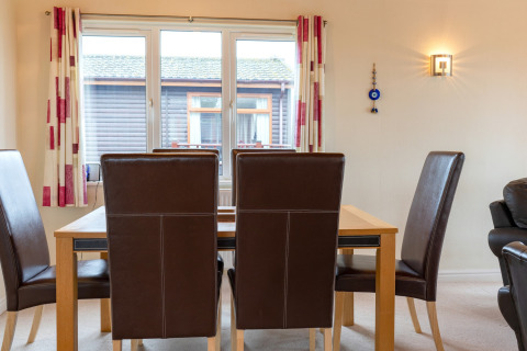 Eethoek in Whitsand Bay Lodge met bruine stoelen, houten tafel, groot raam en lichte gordijnen.
