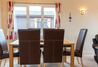 Eethoek in Whitsand Bay Lodge met bruine stoelen, houten tafel, groot raam en lichte gordijnen.