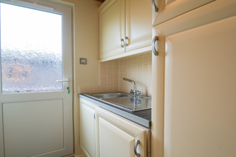 Lichte bijkeuken in Whitsand Bay Lodge met gootsteen, kasten en een deur met matglas.