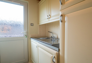 Lichte bijkeuken in Whitsand Bay Lodge met gootsteen, kasten en een deur met matglas.