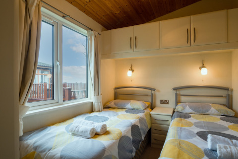 Moderne slaapkamer in Whitsand Bay Lodge UK met twee eenpersoonsbedden, groot raam en zachte verlichting.