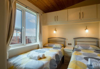 Moderne slaapkamer in Whitsand Bay Lodge UK met twee eenpersoonsbedden, groot raam en zachte verlichting.