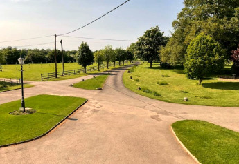 Allée pittoresque d’un site de glamping entourée de pelouses, d’arbres et de jardins verdoyants.
