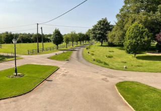 Oprit bij glamping-accommodatie met groene grasvelden, bomen en landelijke sfeer op een zonnige dag.