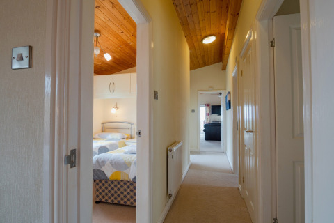 Lichte gang met houten plafond bij Whitsand Bay Lodge, Verenigd Koninkrijk, met zicht op slaapkamers.