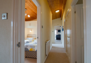 Lichte gang met houten plafond bij Whitsand Bay Lodge, Verenigd Koninkrijk, met zicht op slaapkamers.