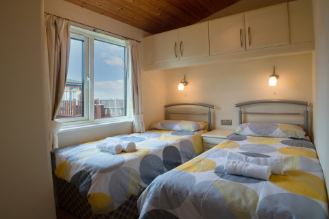 Twee eenpersoonsbedden met kleurrijk dekbed in een lichte kamer bij Whitsand Bay Lodge, Verenigd Koninkrijk.