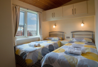 Twee eenpersoonsbedden met kleurrijk dekbed in een lichte kamer bij Whitsand Bay Lodge, Verenigd Koninkrijk.