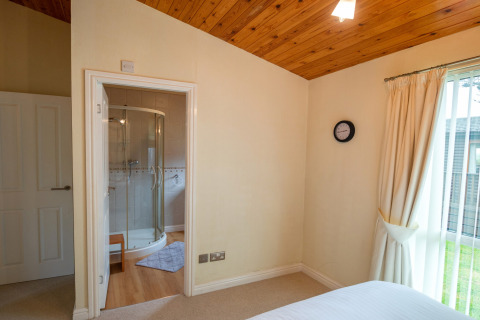 Slaapkamer bij Whitsand Bay Lodge met ensuite badkamer, houten plafond en groot raam met gordijnen.