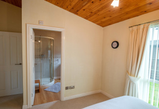 Slaapkamer bij Whitsand Bay Lodge met ensuite badkamer, houten plafond en groot raam met gordijnen.